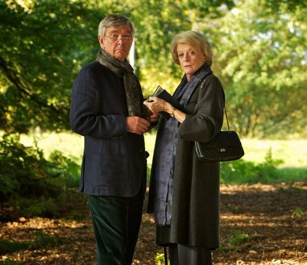 Maggie Smith and a man stood in the woodlands of Hedsor, one of them is holding a book.